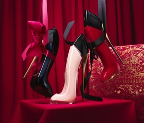 Parfémy Carolina Herrera Good Girl ve tvaru lodiček v černé, růžové a červené barvě na červeném svátečním pozadí s luxusní dárkovou krabicí.