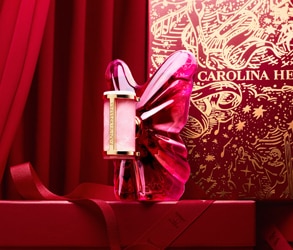 Parfém Carolina Herrera ve tvaru růžového motýla na červeném svátečním pozadí s luxusní dárkovou krabicí.