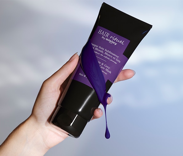 Maska na vlasy Hair Rituel by Sisley pro blond a šedé odstíny v černé tubě s fialovým pigmentem, držená v ruce.