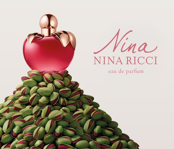 Nina Ricci Nina Eau de Parfum, ikonický flakon ve tvaru jablka v růžové barvě na dekorativním pozadí.
