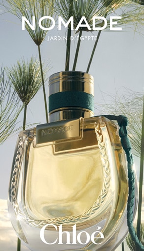 Tři flakony parfému Chloé Nomade Jardin d’Égypte ve zlatém designu na přírodním pozadí.